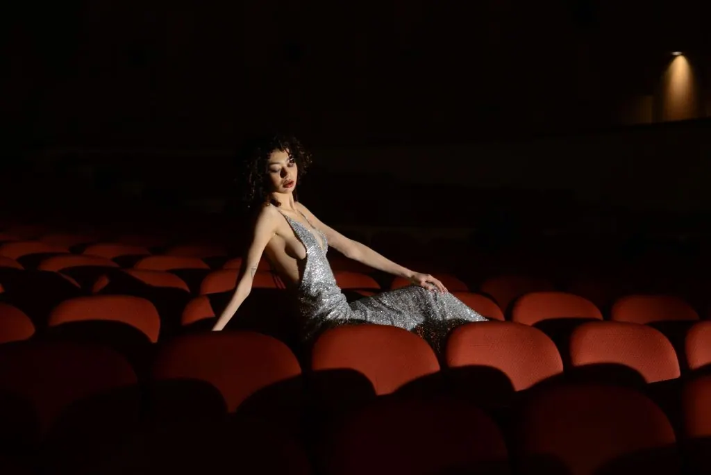 Elegant woman in silver dress sitting in a dimly lit theatre, Mar del Plata, Argentina.