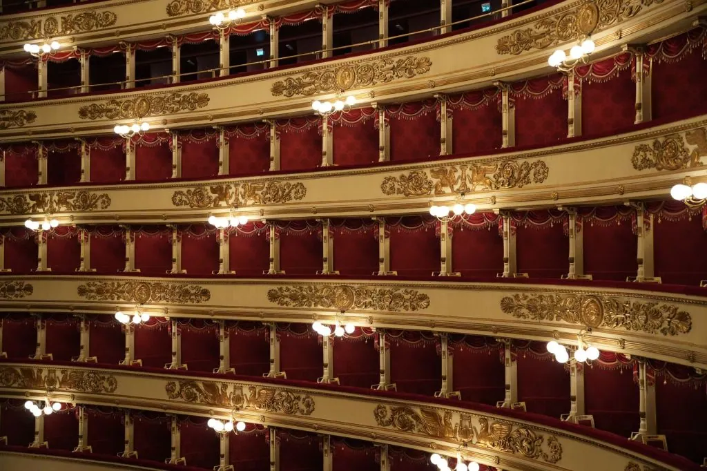 Detailed view of ornate balconies in a historic opera house in Italy, showcasing intricate design and vibrant red decor.