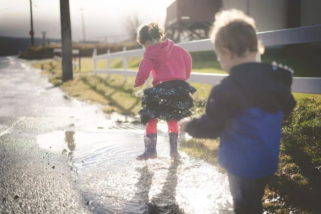 Two children joyfully splashing in a puddle, enjoying a sunny day outdoors.
