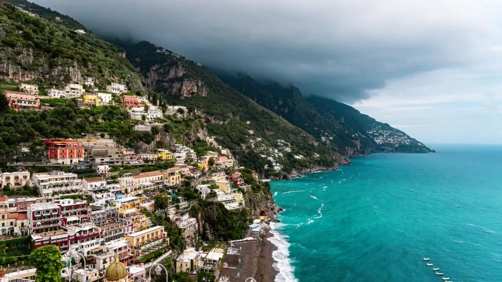 A breathtaking aerial view of Positano's colorful houses on cliffs by the Tyrrhenian Sea under a cloudy sky.