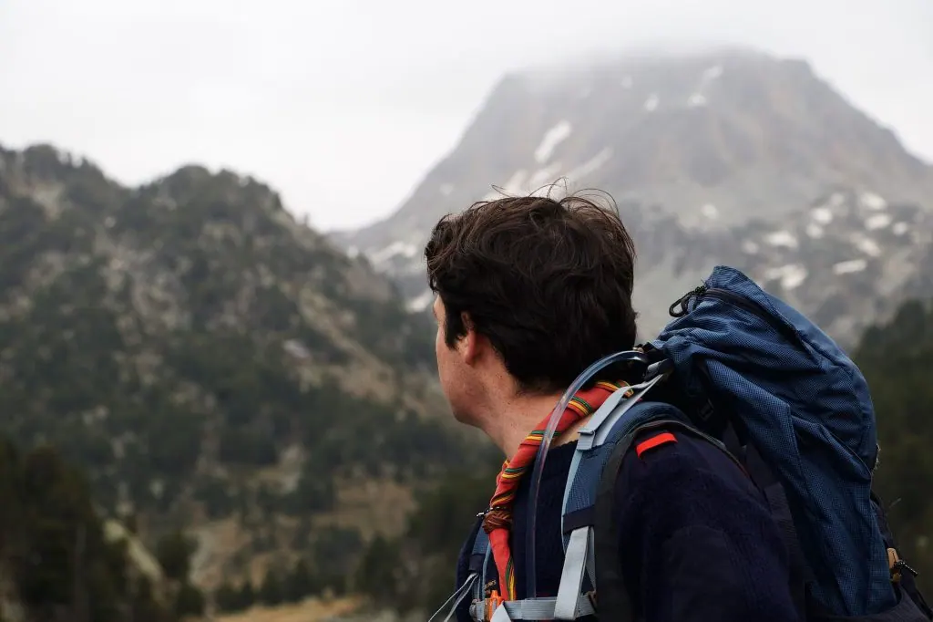 A man with a backpack hiking and enjoying mountainous scenery.