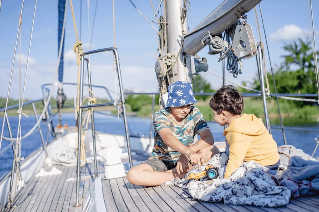 Two boys playing on a sailboat deck under a bright sky in Kherson, enjoying their summer adventure.