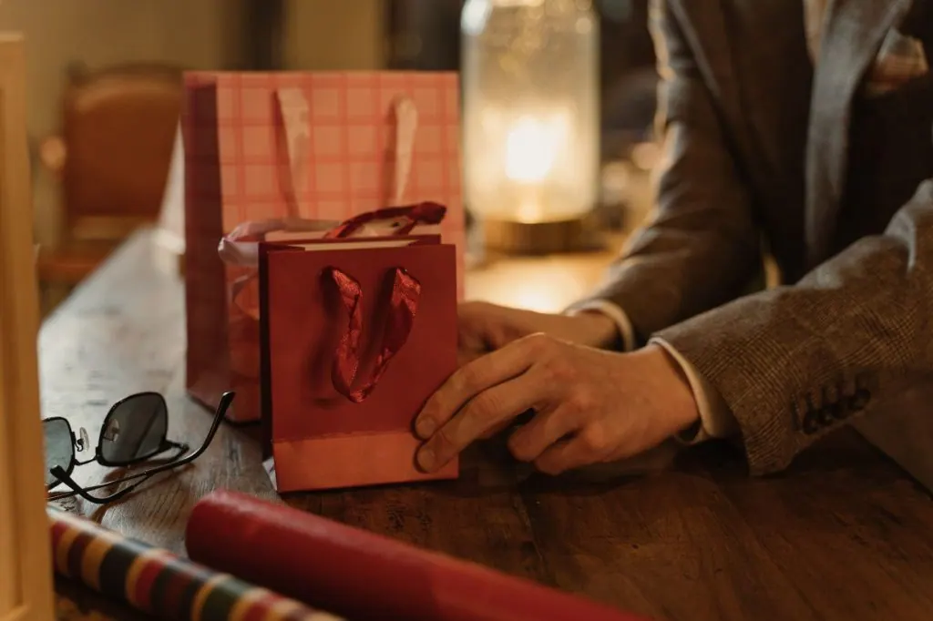 Close-up of hands arranging gift bags on a wooden table, ideal for commerce and business themes.