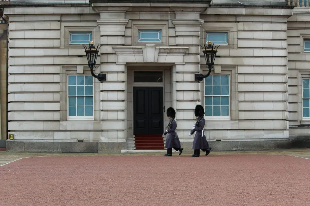 Two royal guards in traditional attire march at Buckingham Palace, London.
