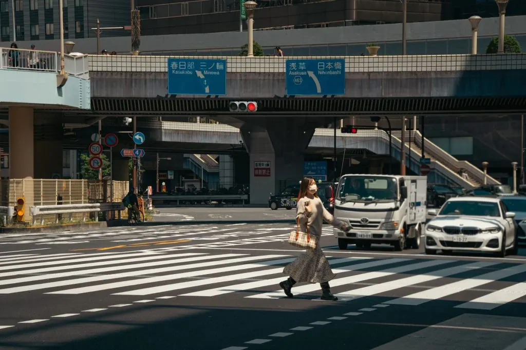 A woman in Tokyo crosses a busy street under a clear sky, highlighting urban life and traffic.