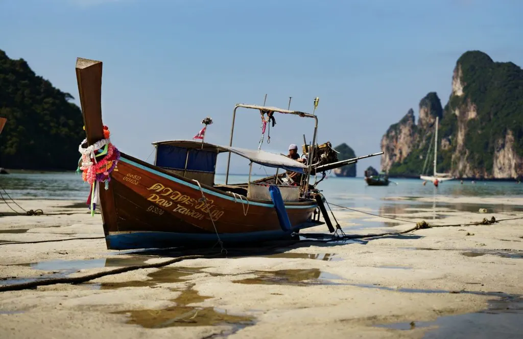 Serene view of a traditional Thai longtail boat on Krabi's beachfront during low tide.