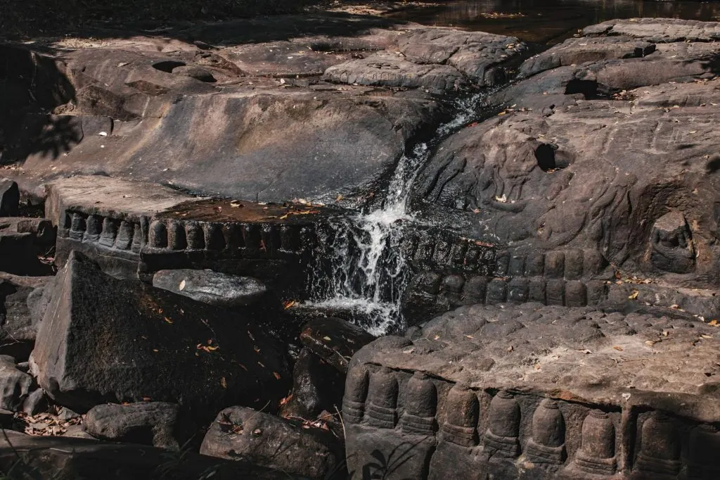 Detailed ancient stone carvings at Kbal Spean waterfall in Cambodia's serene outdoors.