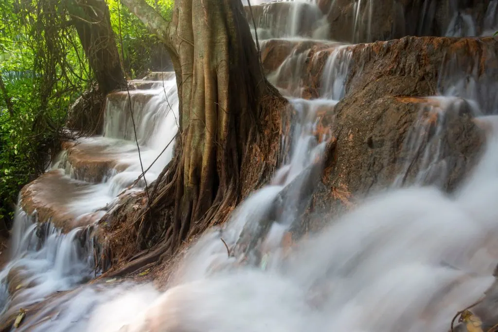 Tranquil waterfall tumbling over rocky steps surrounded by lush greenery in a forest setting.